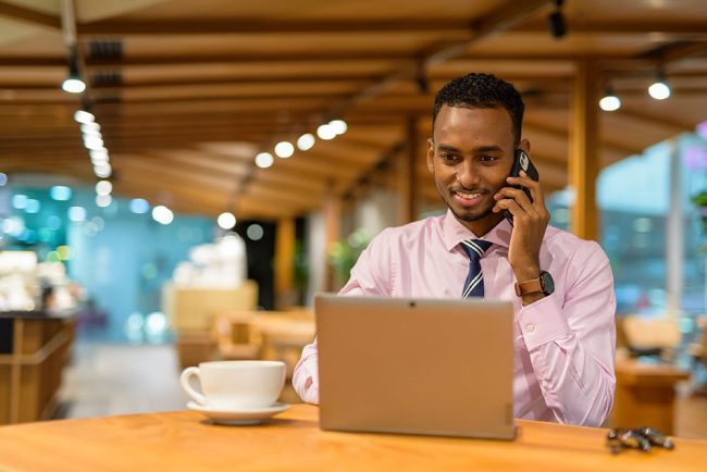 Young African businessman in coffee shop using laptop computer